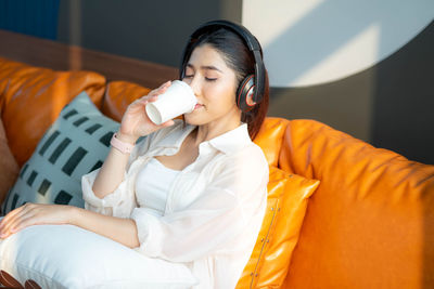 Portrait of young woman drinking milk while sitting on sofa at home