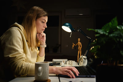 Woman works at home office at night, using laptop