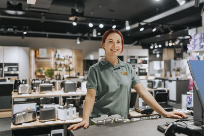 Portrait of smiling female sales clerk standing at counter in electronics store