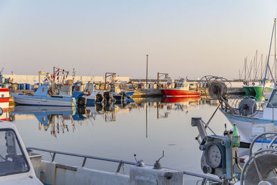 Boats moored in harbor at sunset