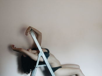 Side view of woman wearing bikini while leaning on ladder against wall