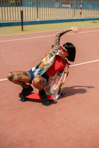 Caucasian girl with tattoos and short black hair on a sports court skating with a skateboard