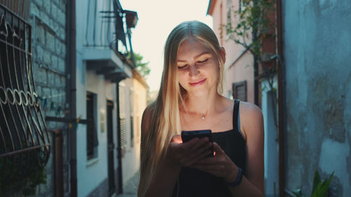 Young woman using smart phone while standing amidst buildings