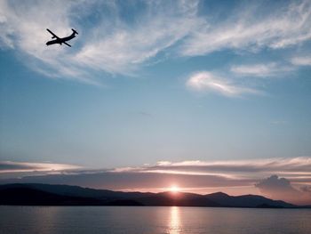 Scenic view of plane flying over sea against cloudy sky