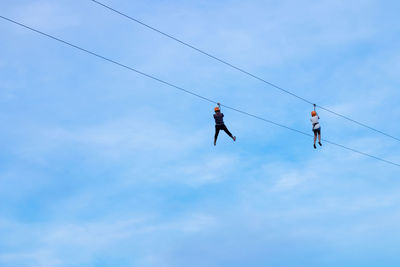 Low angle view of people hanging from ropes against blue sky