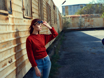 Side view of young woman photographing while standing against building