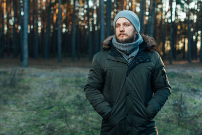 Thoughtful man standing with hands in pockets at forest