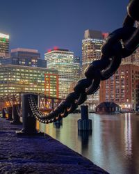 Close-up of metallic chain on pier against illuminated buildings in city at night