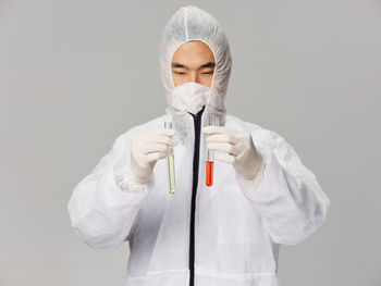 Portrait of young woman wearing surgical mask against white background