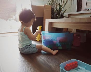 Girl playing with block toys while sitting on hardwood floor at home