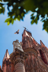 Low angle view of bird perching on roof against clear sky