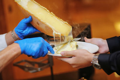 Cropped hands of cheesemonger serving cheese to customer in plate