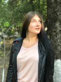 Thoughtful young woman standing against trees