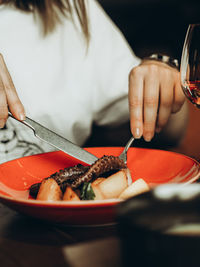 Fried octopus with potatoes on red plate in restaurant. hands of young uncertain woman with cutlery.