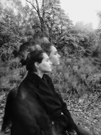 Side view of young woman looking away against trees