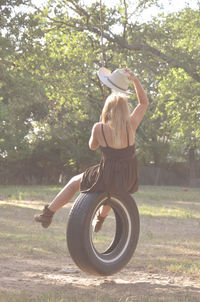 Rear view of woman sitting on tire swing at field