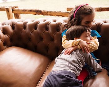 Sister embracing brother while sitting on sofa