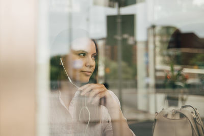 Thoughtful businesswoman wearing headphones seen through glass window at office