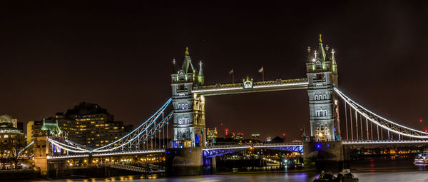 Illuminated bridge over river in city at night