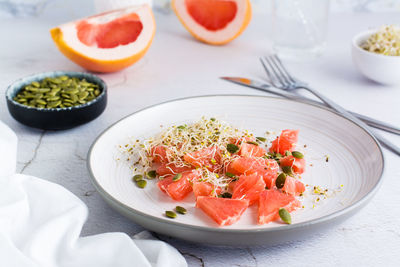 Fresh salad of grapefruit, clover and alfalfa sprouts and pumpkin seeds on a plate on the table. 