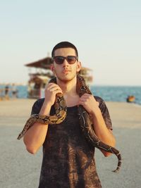 Portrait of young woman with snake wearing sunglasses standing at beach