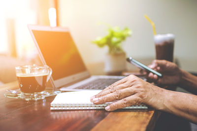 Cropped hands using mobile phone by laptop at table