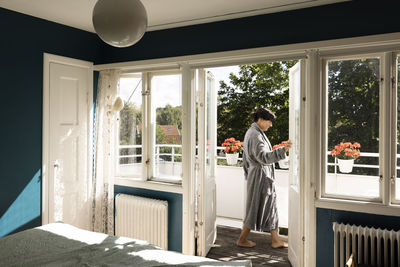 Side view of smiling woman wearing bathrobe while opening balcony door