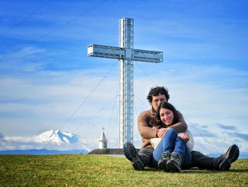 Full length portrait of happy friends sitting on field against sky