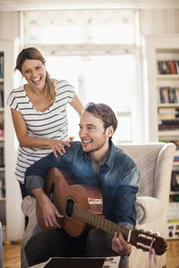 Happy man playing guitar for woman in house