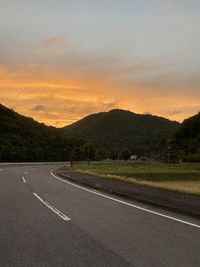 Road by mountains against sky during sunset