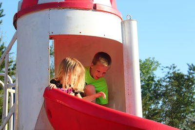 Low angle view of siblings on slide at playground