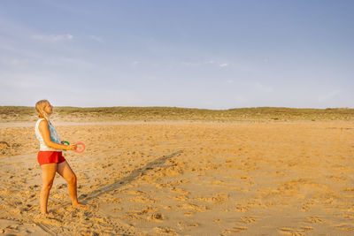 Side view of woman playing at beach against sky