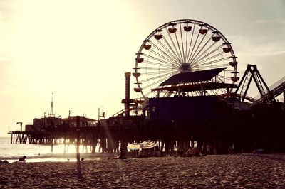 Ferris wheel on beach against sky during sunset