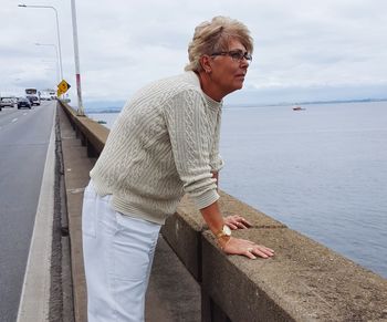 Man standing on retaining wall by sea against sky