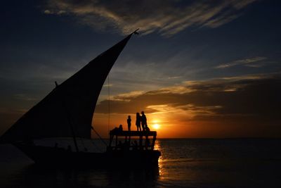 Silhouette people on sailboat in sea against sky during sunset