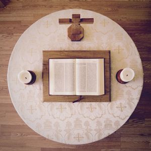 Top view of open bible book by candles and cross shape on wooden table