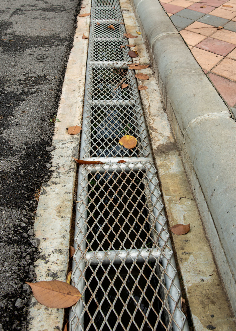 HIGH ANGLE VIEW OF METAL GRATE ON FOOTPATH