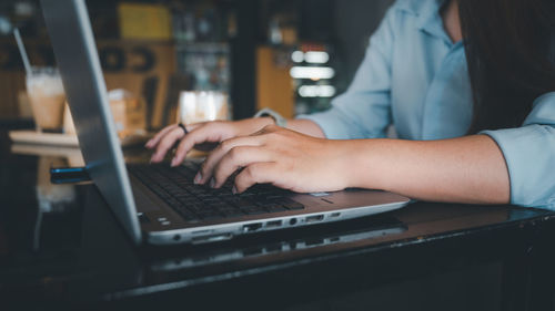 Midsection of woman using laptop on table in cafe