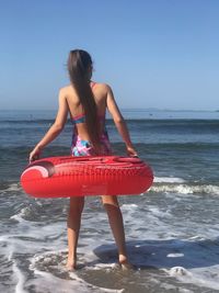 Rear view of girl with inflatable ring standing at shore against clear sky