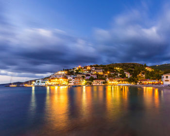 Illuminated buildings by sea against sky at night