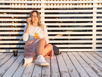 Young woman sitting on wooden wall