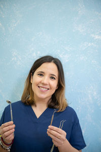 Portrait of smiling dentist holding medical equipment against wall