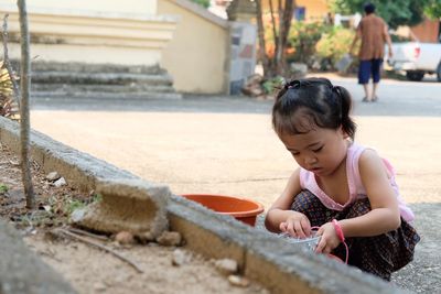 Girl playing with bowl while crouching on street