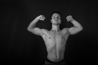 Portrait of shirtless man standing against black background