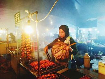 Young woman standing by illuminated lighting equipment