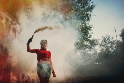 Low angle view of woman holding distress flare against trees