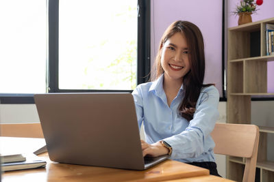 Portrait of smiling woman using phone while sitting on table