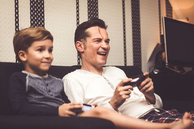 Father with son playing video game while sitting on sofa at home