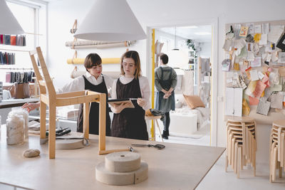 Female upholstery workers reading note pad with chair on desk in workshop