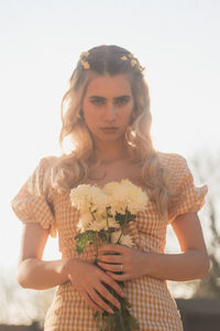 Low angle portrait of beautiful woman holding flowers against clear sky